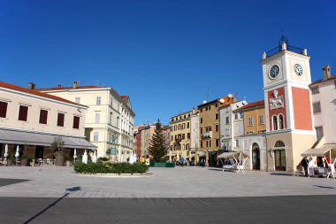 ROVINJ, CROATIA - 1 Aralık 2024: Hırvatistan 'ın renkli binalarıyla çevrili bronz bir fıskiye heykeli bulunan güneşli kasaba meydanı