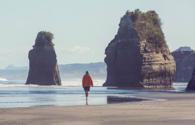 Yeni Zelanda 'nın Yeni Plymouth kıyısındaki Üç Kız Kardeş kaya oluşumunda sahilde yürüyen bir turist.