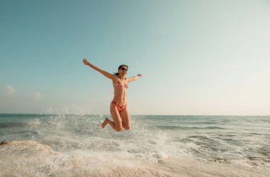 Deniz sahilinde dalgalarda oynayan genç bir kadın.