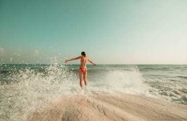 Deniz sahilinde dalgalarda oynayan genç bir kadın.