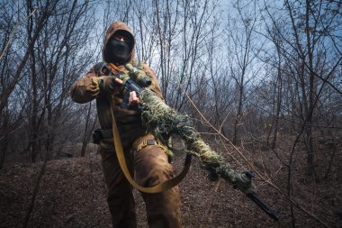 Keskin nişancı ormanın içinde tüfek yürüyüş ile kamuflaj takım elbise