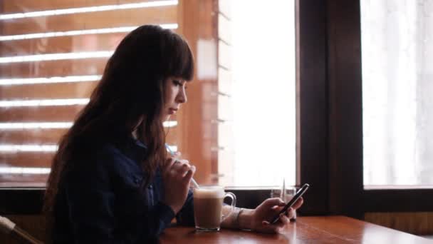 Chica joven usando el teléfono inteligente en el café — Vídeos de Stock