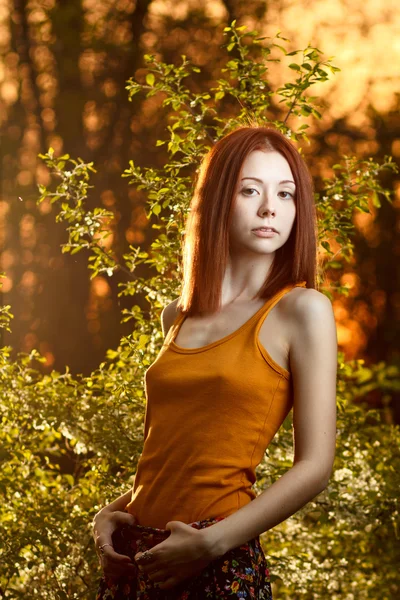 Redhead girl walking under sunset rays in forest — Stock Photo, Image