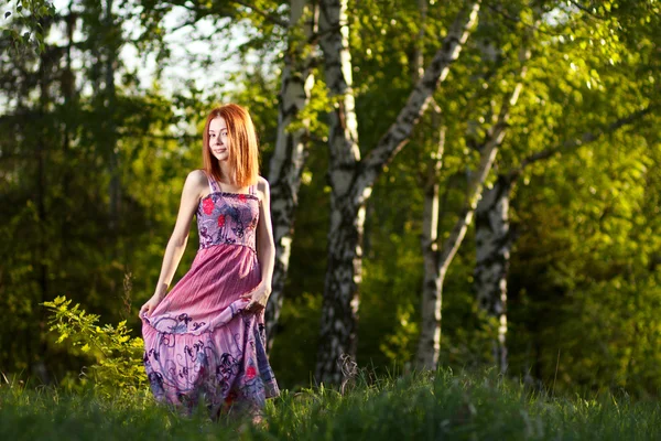 Рыжая девушка гуляет под лучами закатного леса — стоковое фото