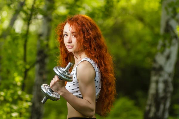Redhead girl exercising with dumbbells at forest — Stock Photo, Image