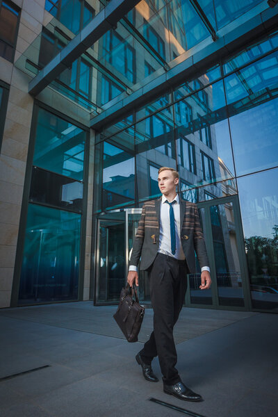 Young handsome successful stylish businessman walking near modern office