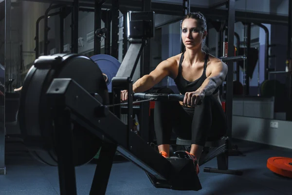 çekici kaslı kadın Crossfit eğitmen kapalı kürekçi üzerinde egzersiz yapmak