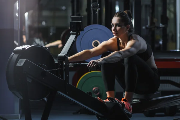 Attraente donna muscolare CrossFit allenatore fare allenamento su vogatore indoor — Foto Stock