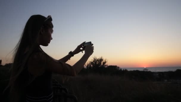 Dívka, vyfotit se s telefonem při západu slunce — Stock video