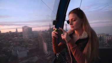 Seyahat: güzel genç kadın turist camdan bakarak, gün batımında ropeway kabin onu cep telefonu ile fotoğraf yapma. Orta çekim, yavaş çekim 60 fps, el.