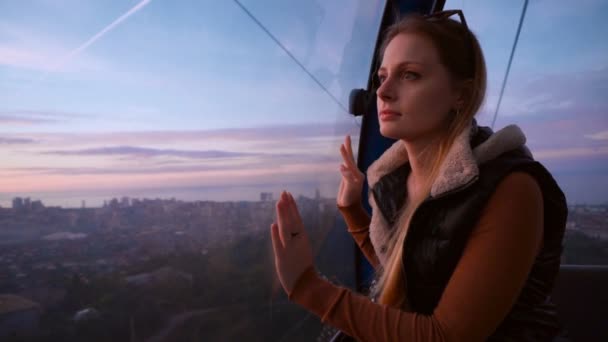 Reise: Schöne junge Touristin blickt durch das Glas und macht Fotos mit ihrem Handy in der Seilbahn bei Sonnenuntergang. Mittlerer Schuss, Handheld. — Stockvideo