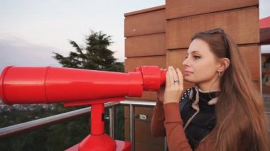 Seyahat: Genç kadın turist gün batımında sikke ile işletilen dürbün ile şehre bakıyor. Orta çekim, el, yavaş çekim 60fps