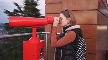 Seyahat: Genç kadın turist gün batımında sikke ile işletilen dürbün ile şehre bakıyor. Orta çekim, el, yavaş çekim 60fps