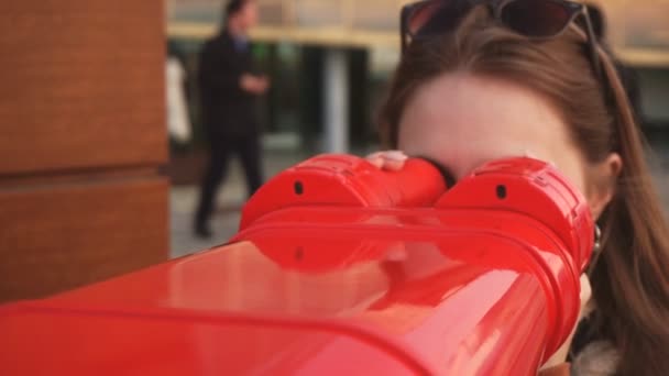 Travel: young woman tourist looking at city through coin-operated binoculars at sunset. Close-up shot, handheld, slow motion 60fps — Stock Video