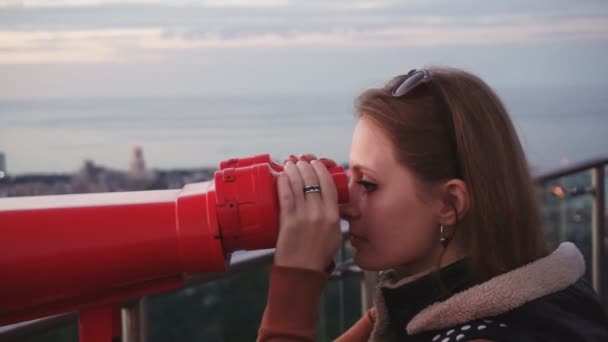 Viajes: turista joven mirando a la ciudad a través de prismáticos operados con monedas al atardecer. Primer plano, de mano, cámara lenta 60fps — Vídeos de Stock