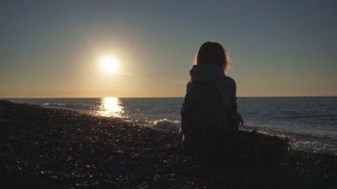 Seyahat: Gün batımında plajda oturma güzel kız turist silueti. Geniş çekim, yavaş çekim 60fps, el.