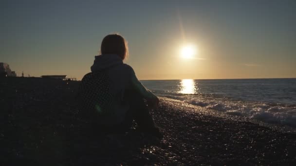 Utazás: Silhouette gyönyörű lány turisztikai ülések a tengerparton naplementekor. Széles lövés, lassított 60fps, statikus. — Stock videók