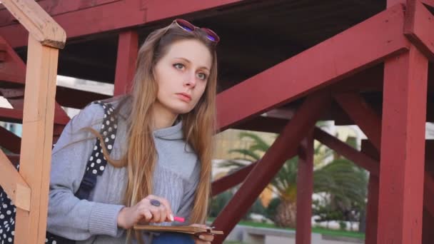 Travel: beautiful girl tourist drawing sunset at the beach. Medium shot, slow motion, handheld. — Stock Video