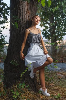 Fashion portrait shoot of beautiful teen girl posing near tree