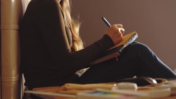 Estilo de vida: jovem menina bonita designer artista freelance esboçando e desenho em papel kraftpaper em casa durante o pôr do sol. Tiro médio, estático, câmera lenta 60 fps . — Vídeo de Stock