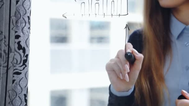 Красивая молодая женщина рисует бизнес-графики на стекле с небоскребом на заднем плане. Крупный план, статический . — стоковое видео