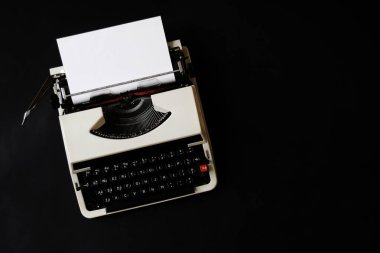 Üst görünüm, eski daktilo makinesinin düz yatay fotoğrafını siyah arkaplanda fotokopi alanı ile birlikte beyaz boş kağıt ile kapat