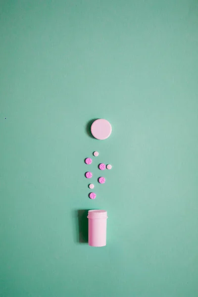 コピースペース付きの明るい緑の背景にピンクと白の錠剤とオープンボトルの現代的なミニマリストの写真 — ストック写真