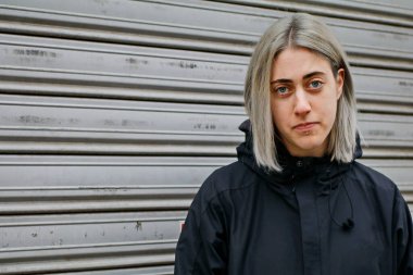Metal arka planda siyah giyinmiş gümüş saçlı bir kızın portresi.