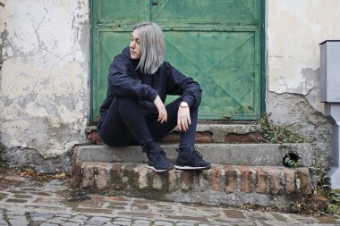 Siyah elbiseli kız eski evin önünde oturuyor.