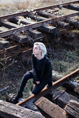 Terk edilmiş tren istasyonunda poz veren siyahlı yakışıklı bir adam.