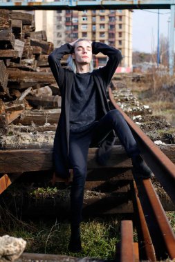 Terk edilmiş tren istasyonunda poz veren siyahlı yakışıklı bir adam.