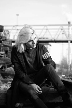 Terk edilmiş tren istasyonunda poz veren siyahlı yakışıklı bir adam.