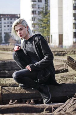 Terk edilmiş tren istasyonunda poz veren siyahlı yakışıklı bir adam.