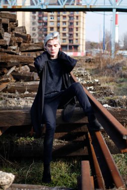 Terk edilmiş tren istasyonunda poz veren siyahlı yakışıklı bir adam.