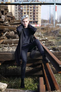 Terk edilmiş tren istasyonunda poz veren siyahlı yakışıklı bir adam.