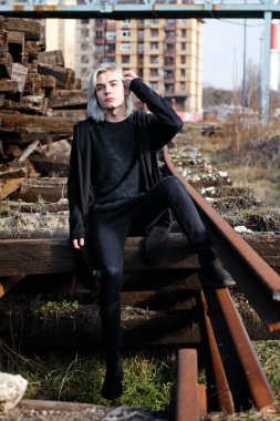 Terk edilmiş tren istasyonunda poz veren siyahlı yakışıklı bir adam.