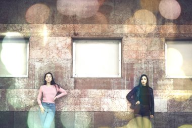 two stylish women posing by old building wall