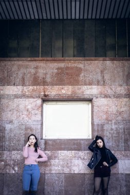 two stylish women posing by old building wall