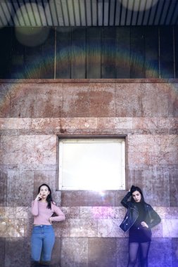 two stylish women posing by old building wall