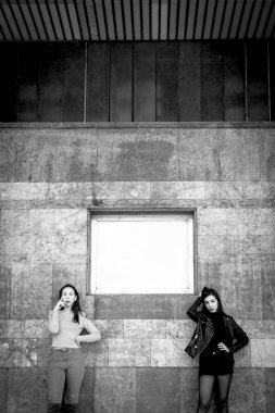 two stylish women posing by old building wall, black and white