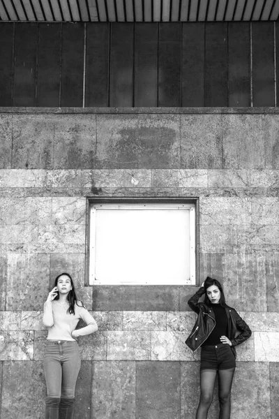 two stylish women posing by old building wall, black and white