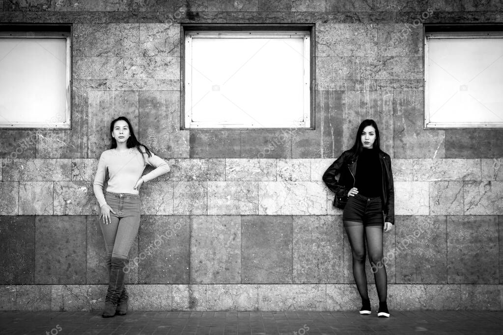 two stylish women posing by old building wall, black and white