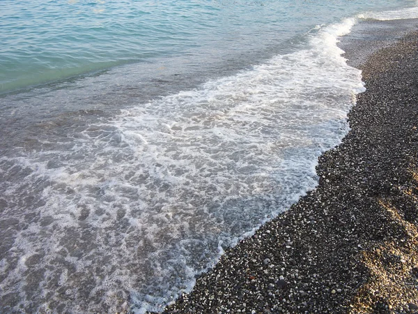 Praia de seixos escuros e onda azul do mar — Fotografia de Stock
