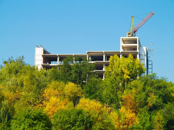Kraan en gebouw bouwplaats tegen blauwe hemel en bomen — Stockfoto
