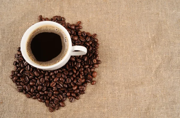 Kaffebönor med mugg på en grov säckväv — Stockfoto