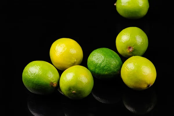 Grüne und gelbe Zitronen auf schwarzem Hintergrund — Stockfoto