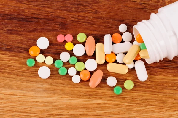 Montón de pastillas cerca del recipiente abierto en el escritorio de madera — Foto de Stock