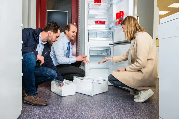 Försäljaren visar kylskåp till par i stormarknad — Stockfoto