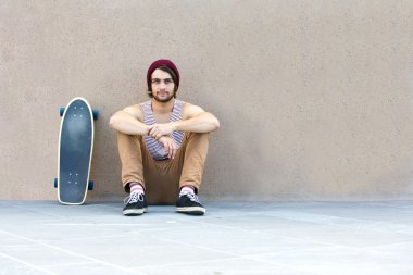 Skateboarder sitting against granite wall clipart