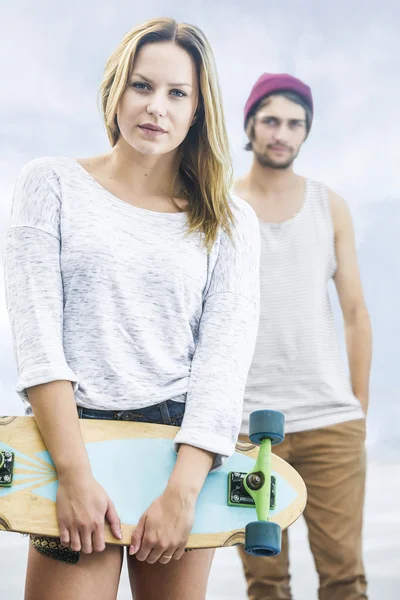 Девушка со скейтбордом перед мальчиком — стоковое фото